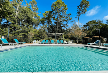 a swimming pool with blue chairs and trees in the background